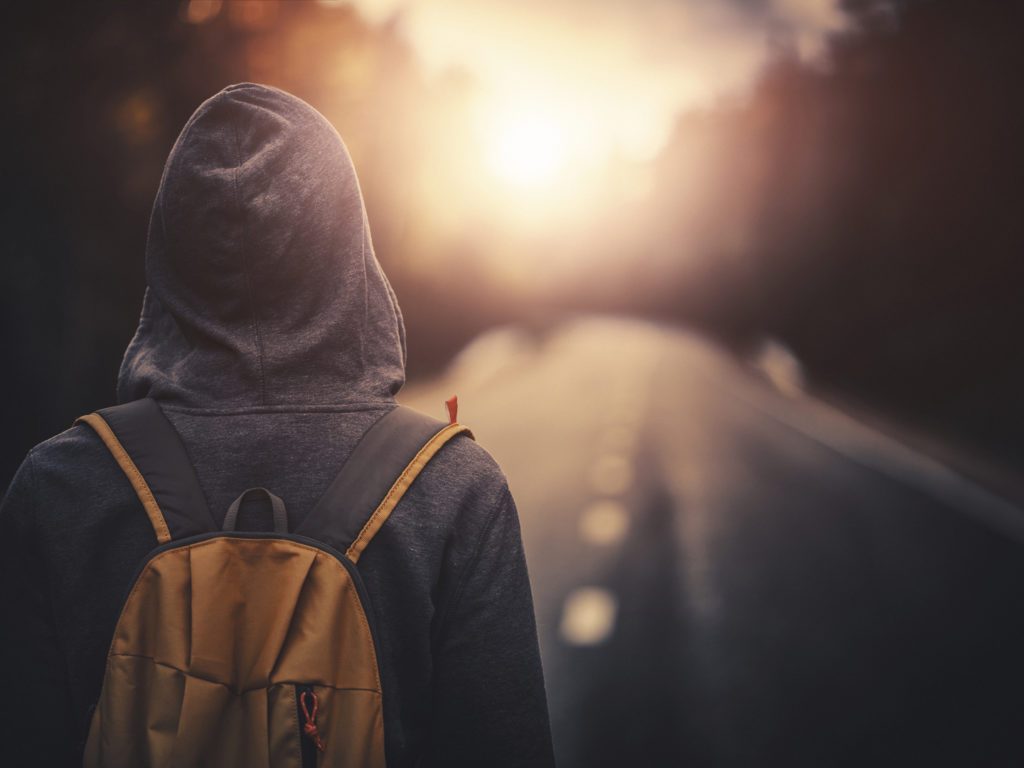 Traveler with backpack walking forward alone at sunset